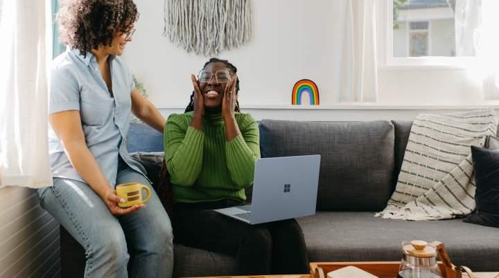 Two women have a conversation, one has a laptop on her knee