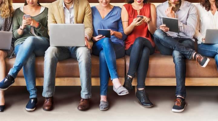 Row of people sat using a range of devices - laptops, ipads, phones. 